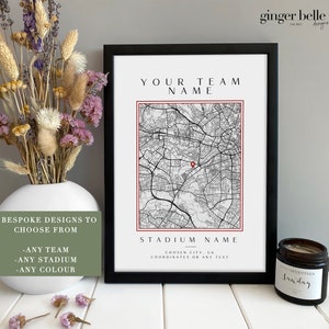 May include: A black framed print with a white background and a black and white map of a city. The map has a red pin in the centre. The text "YOUR TEAM NAME" is at the top of the print. The text "STADIUM NAME" is at the bottom of the print. The text "CHOSEN CITY, UK COORDINATES OR ANY TEXT" is below the stadium name.
