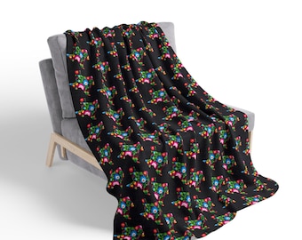 May include: A black throw blanket featuring a repeating pattern of the state of Texas filled with vibrant, multi-colored floral designs in shades of red, blue, green, yellow, and white, draped over a gray upholstered chair.