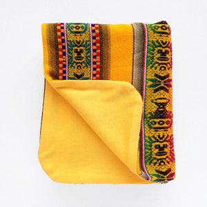 May include: A yellow throw blanket with a colorful geometric pattern on one side and a solid yellow side. The blanket is folded in half and the patterned side is facing up.