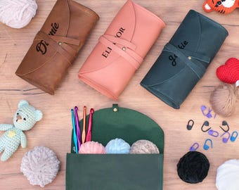 May include: Three personalised leather zippered pouches in brown, pink and green with the names "Dannie", "Ellie" and "Jackie" embroidered on them. The pouches are open and show the inside lining. The green pouch has crochet hooks and yarn balls inside.