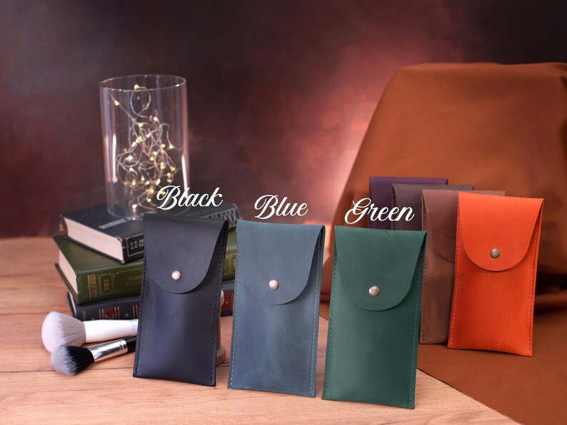 May include: Five leather phone cases in different colors: black, blue, green, brown, and orange. Each case has a flap with a button closure.