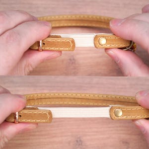 May include: A brown leather collar with a white elastic insert. The collar has a gold metal buckle and a gold metal rivet.