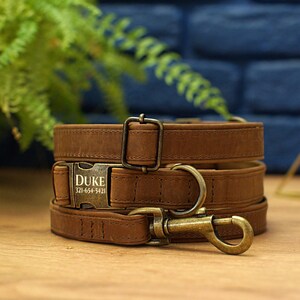 Puede incluir: Conjunto de collar y correa para perro de cuero marr&oacute;n con una etiqueta de metal personalizada que dice "DUKE 321-654-5421".