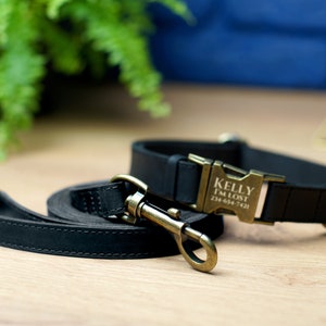 Puede incluir: Conjunto de collar y correa para perro de cuero negro con hebilla dorada. La hebilla tiene el nombre "Kelly" y el texto "I'm Lost" con un n&uacute;mero de tel&eacute;fono grabado.