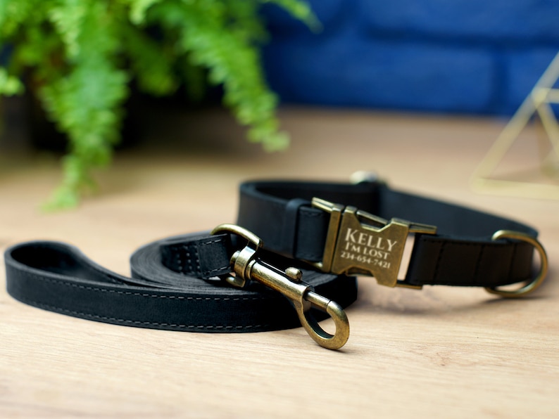 Puede incluir: Conjunto de collar y correa para perro de cuero negro con hebilla dorada. La hebilla tiene el nombre "Kelly" y el texto "I'm Lost" con un n&uacute;mero de tel&eacute;fono grabado.