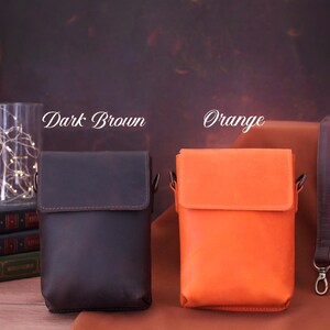 May include: Two leather crossbody bags, one dark brown and one orange, with matching straps. The dark brown bag is on the left, and the orange bag is on the right. The text "Dark Brown" and "Orange" are above the bags.