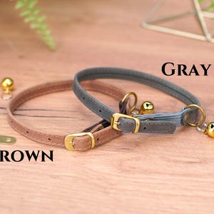 May include: Two cat collars, one brown and one gray, with gold buckles and bells. The collars are on a wooden surface. The text "GRAY" and "BROWN" is visible.