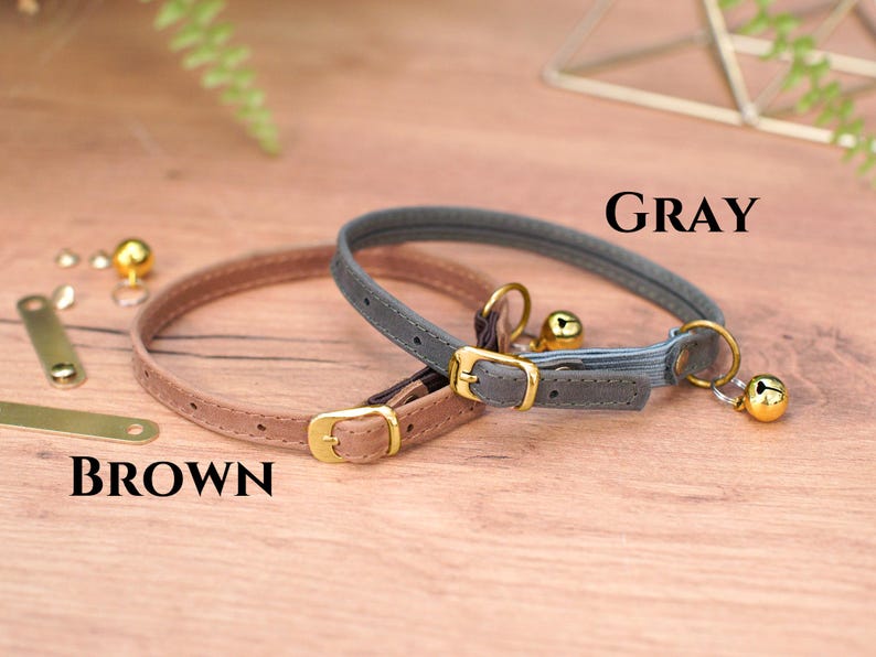 May include: Two cat collars, one brown and one gray, with gold buckles and bells. The collars are on a wooden surface. The text "GRAY" and "BROWN" is visible.