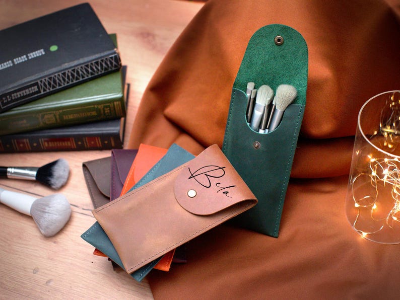 May include: Four leather brush holders, one green, one brown, one orange, and one blue. The brown holder has the word "Bria" written on it. The green holder has five brushes inside.