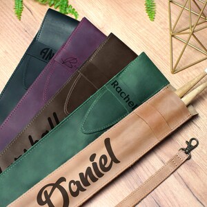 Puede incluir: Cinco estuches para baquetas de cuero en diferentes colores con nombres personalizados:  "Amy", "Rachel", "Marshall", "Daniel".