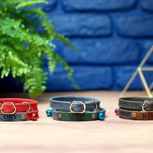 May include: Three leather dog collars with personalized name tags and bells. The collars are red, blue, and brown. The name tags read "Cory I'm chipped", "Copper I'm chipped call my mom", and "Jessie".