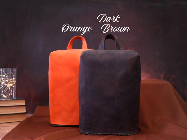 May include: Two rectangular, upright bags with top handles. One is bright orange, the other is dark brown. The bags have a zipper at the base. The text "Orange" and "Dark Brown" is written above the bags.