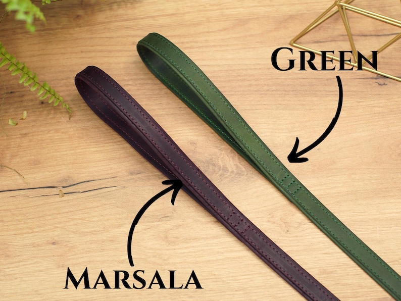 Puede incluir: Dos correas de cuero, una verde y otra morado oscuro, etiquetadas como "GREEN" y "MARSALA" respectivamente. Las correas est&aacute;n sobre una superficie de madera.