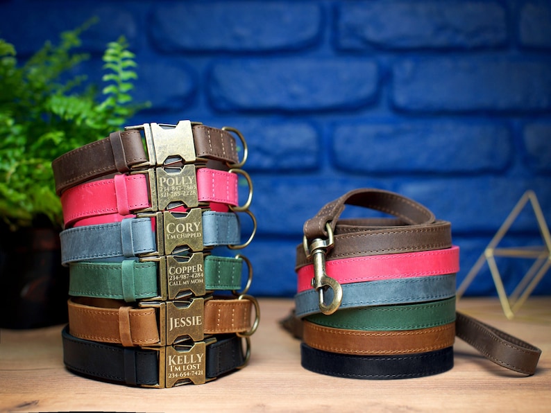 Puede incluir: Pila de seis collares de perro de cuero personalizados en varios colores, incluyendo marr&oacute;n, rosa, gris, verde, marr&oacute;n claro y negro. Cada collar tiene una hebilla de lat&oacute;n y texto grabado con el nombre del perro y un n&uacute;mero de tel&eacute;fono. Tambi&eacute;n se muestra una correa de perro de cuero marr&oacute;n.