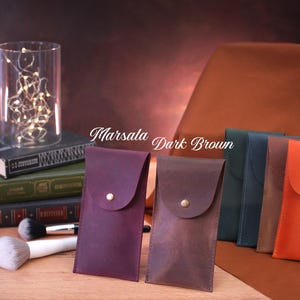 May include: Four leather pouches in different colors, including marsala, dark brown, navy blue, and orange. The pouches have a flap with a button closure. The text "Marsala Dark Brown" is written on the image.