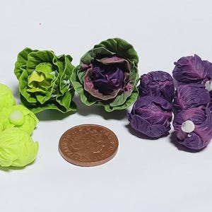 May include: A collection of miniature cabbages in green and purple, alongside a penny for scale. The green cabbages are a vibrant hue, and the purple ones are a deep shade. These cabbages are likely for a dollhouse or miniature display.