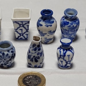 Puede incluir: Una colección de ocho jarrones de porcelana azul y blanca en miniatura con varios diseños florales y geométricos. Los jarrones están dispuestos sobre una superficie blanca.