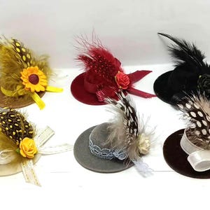 Peut inclure: Plusieurs chapeaux miniatures ornés de plumes, de rubans et de fleurs. Les chapeaux sont de différentes couleurs, notamment marron, rouge, noir et gris. Certains présentent un tournesol ou une rose.