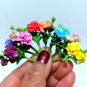 Könnte beinhalten: Ein Strauß aus künstlichen Miniaturblumen in verschiedenen Farben, darunter Rosa, Lila, Blau, Gelb, Orange und Rot. Die Blumen sind fächerförmig angeordnet und werden in einer Hand gehalten.
