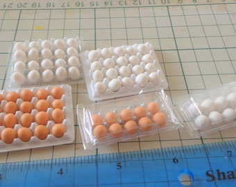 May include: Four containers of miniature plastic eggs. Two containers are white with brown eggs, one container is white with white eggs, and one container is clear plastic with white eggs. A blue ruler with the words "Shatter R" is in the bottom right corner of the image.