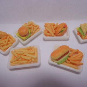 Könnte beinhalten: Miniatur-Fastfood-Artikel, darunter ein Burger, ein Sandwich, ein Croissant und Pommes Frites, angeordnet auf kleinen weißen Tabletts. Die Lebensmittel sind detailliert mit realistischen Farben und Texturen, wodurch eine spielerische, essensbezogene Präsentation entsteht.