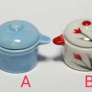 May include: Two miniature ceramic pots, one light blue with a lid and the other white with red tulip designs. The pots are labelled A and B.