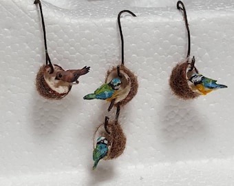Può includere: Tre casette per uccelli in miniatura realizzate con gusci di cocco, ciascuna con una piccola statuetta di uccello all'interno. Le casette per uccelli sono appese a una superficie bianca.