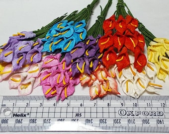 May include: A bunch of 24 paper calla lily flowers in various colors, including yellow, purple, pink, blue, white, and red. The flowers are approximately 2 inches in length and are arranged on a white surface with a ruler for scale.