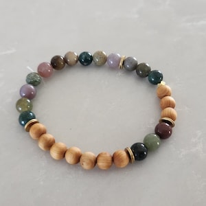 May include: A bracelet made of wooden beads and green, purple, and brown gemstone beads with gold accents.