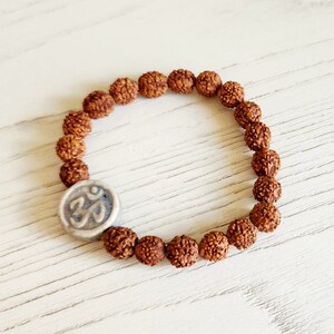 May include: A brown wooden bracelet with a silver Om charm. The bracelet is made of small, round beads.