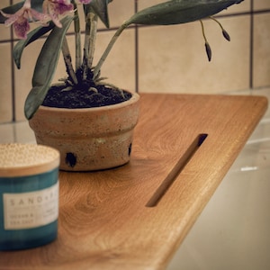 Peut inclure: Un plateau de bain en bois avec une fente pour un savon. Une plante d'orchidée en pot avec des fleurs roses est posée sur le plateau, à côté d'une bougie bleue.