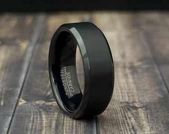 May include: A black tungsten carbide ring with a beveled edge and a brushed finish. The ring has the words "Tungsten Carbide" engraved on the side.