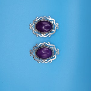 May include: A pair of silver earrings with ornate designs and purple oval-shaped stones.