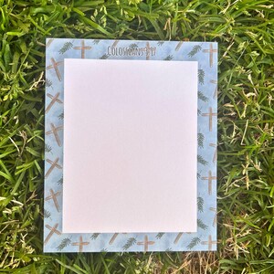 May include: A blue and white notepad with a border of brown crosses and green leaves. The text "Colossians 3:17" is printed at the top of the notepad.