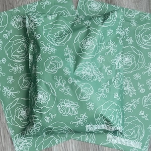 May include: Two green mailing envelopes with a white floral pattern and the text "I'm Biodegradable" printed on the bottom.