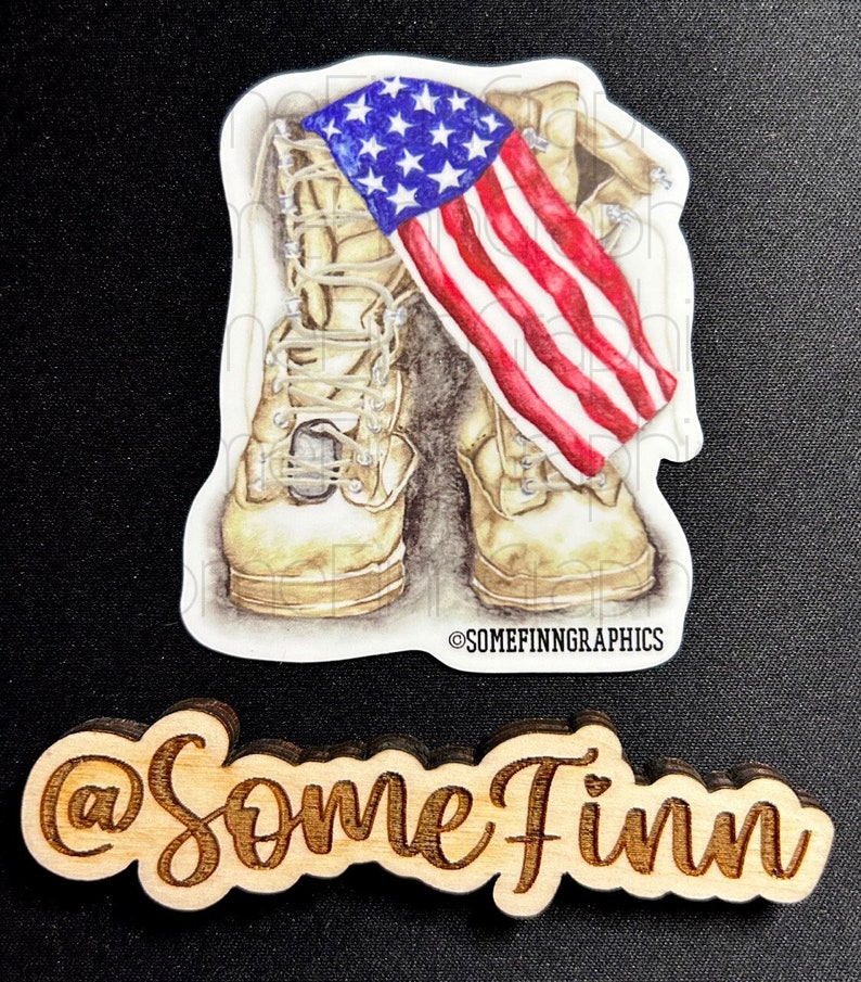 May include: A sticker featuring a pair of tan military boots with an American flag draped over them. The flag is red, white, and blue with white stars on a blue field. The sticker has the text "@SomeFinnGraphics" at the bottom.