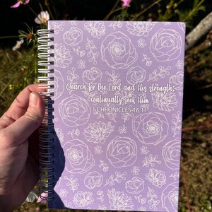 May include: A purple spiral bound notebook with a white floral pattern and the text "Search for the Lord and His strength; continually seek Him 1 CHRONICLES 16:11"
