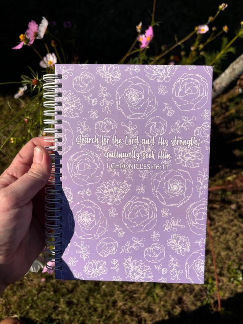 May include: A purple spiral bound notebook with a white floral pattern and the text "Search for the Lord and His strength; continually seek Him 1 CHRONICLES 16:11"
