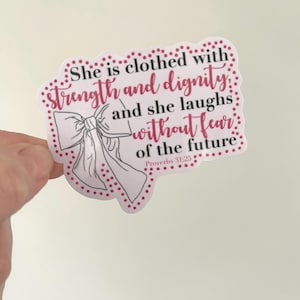 May include: A sticker with a scalloped edge and a bow illustration. The sticker features the text "She is clothed with strength and dignity and she laughs without fear of the future. Proverbs 31:25" in pink and black.