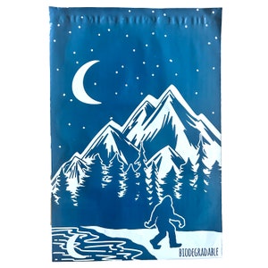 May include: A blue biodegradable mailing envelope with a white design of a mountain range, a crescent moon, and a Bigfoot walking in front of a lake. The text "BIODEGRADABLE" is printed in white at the bottom of the envelope.
