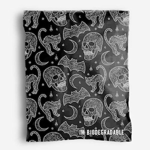 Könnte beinhalten: Schwarz-weißes sich wiederholendes Muster mit Totenköpfen, Fledermäusen, Mondsicheln und Katzen. Das Muster ist auf schwarzem Hintergrund und das Design ist weiß. Der Text "IM BIODEGRADABLE" befindet sich am unteren Rand des Bildes.