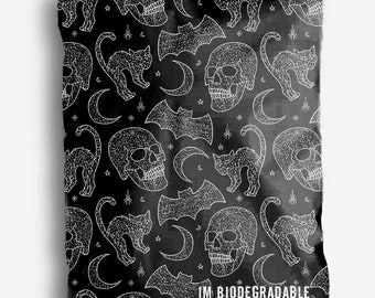 May include: Black and white repeating pattern featuring skulls, bats, crescent moons, and cats. The pattern is on a black background and the design is white. The text "IM BIODEGRADABLE" is at the bottom of the image.