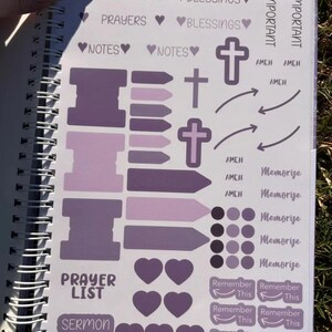 May include: A purple and white planner with stickers for prayer, blessings, and sermon notes. The stickers include crosses, arrows, hearts, and circles.