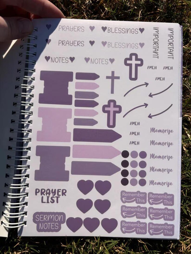 May include: A purple and white planner with stickers for prayer, blessings, and sermon notes. The stickers include crosses, arrows, hearts, and circles.