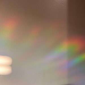 May include: A white wall with a rainbow prism light reflection. The light creates a colorful, blurry, and abstract pattern on the wall.
