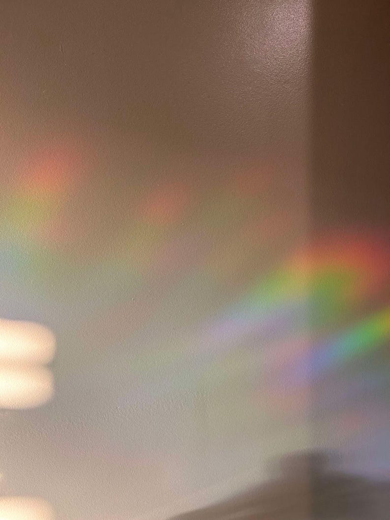 May include: A white wall with a rainbow prism light reflection. The light creates a colorful, blurry, and abstract pattern on the wall.