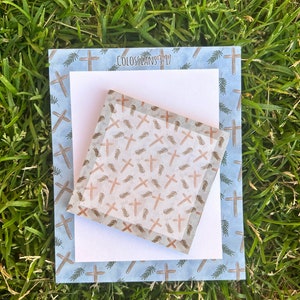 May include: A blue notepad with a white sheet of paper on top. Both sheets have a pattern of brown crosses and green leaves. The top sheet has the text "Colossians 3:17" printed on it.