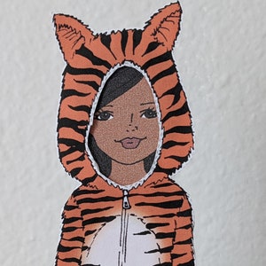 May include: A child wearing a tiger costume with orange and black stripes. The costume has a hood with ears and a zip in the front.