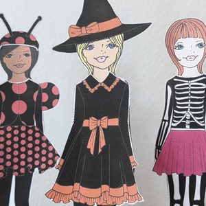 May include: Three paper dolls dressed in Halloween costumes. The doll on the left is wearing a ladybug costume with black and red polka dots. The doll in the middle is wearing a witch costume with a black dress, orange trim, and a black witch hat. The doll on the right is wearing a skeleton costume with a black and white striped shirt and a pink skirt.