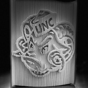 May include: A black and white book art sculpture of a stylized dragon with intricate details. The sculpture is made by folding pages of a book.